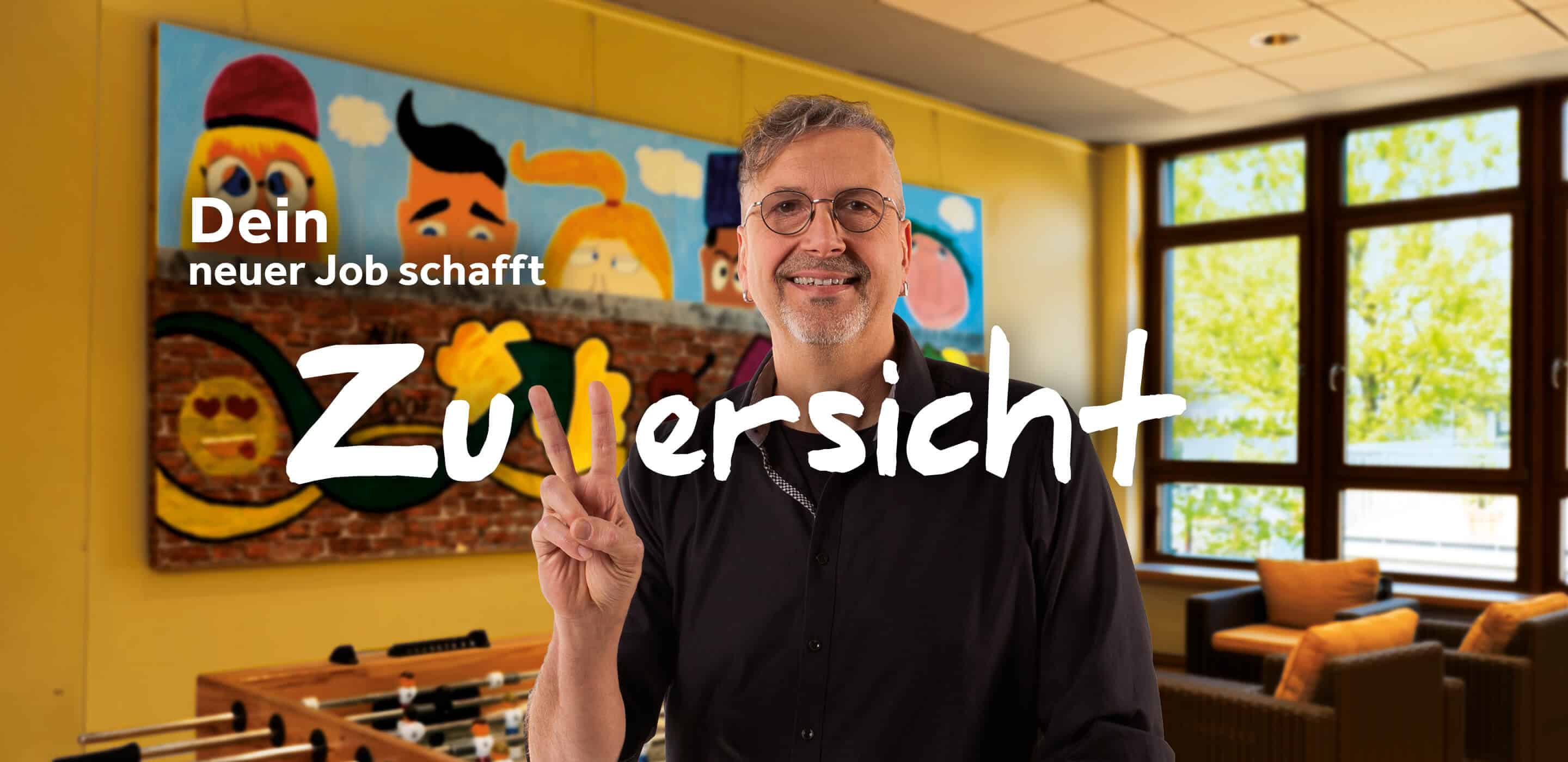 Mann zeigt ein Peace-Zeichen vor einem Kicker im Aufenthaltsraum. Motiv wirbt für Jobs beim Kreis Viersen.