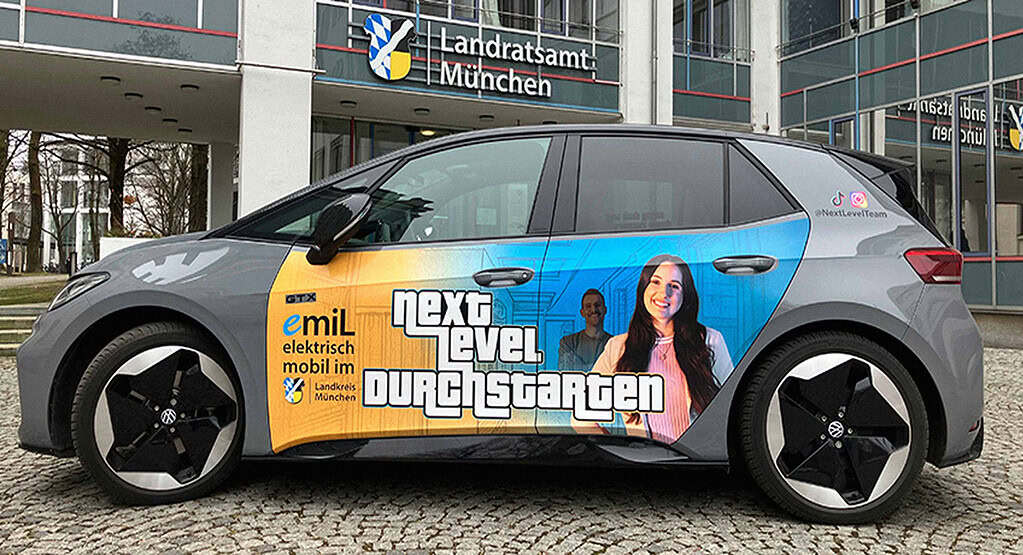 Elektroauto des Landkreises München mit „Next Level durchstarten“-Beklebung vor dem Landratsamt München.